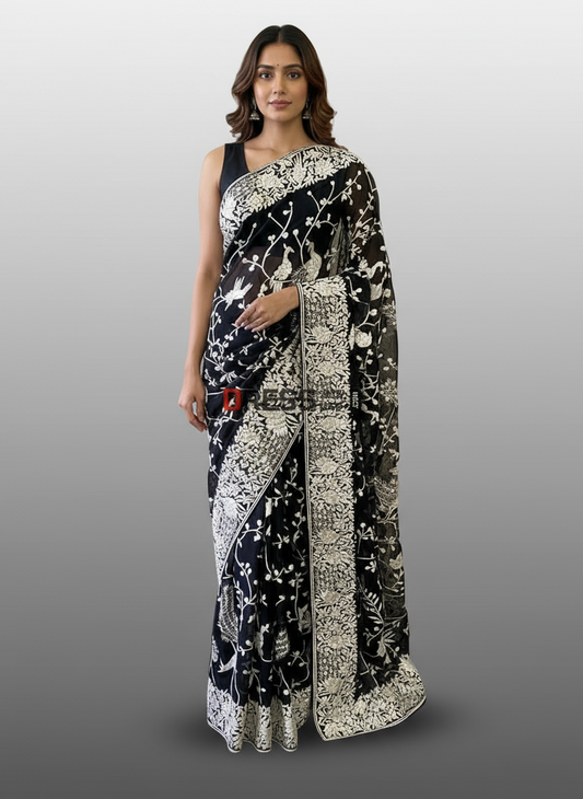 Woman wearing a Parsi Gara black and white saree against a beige textured wall.